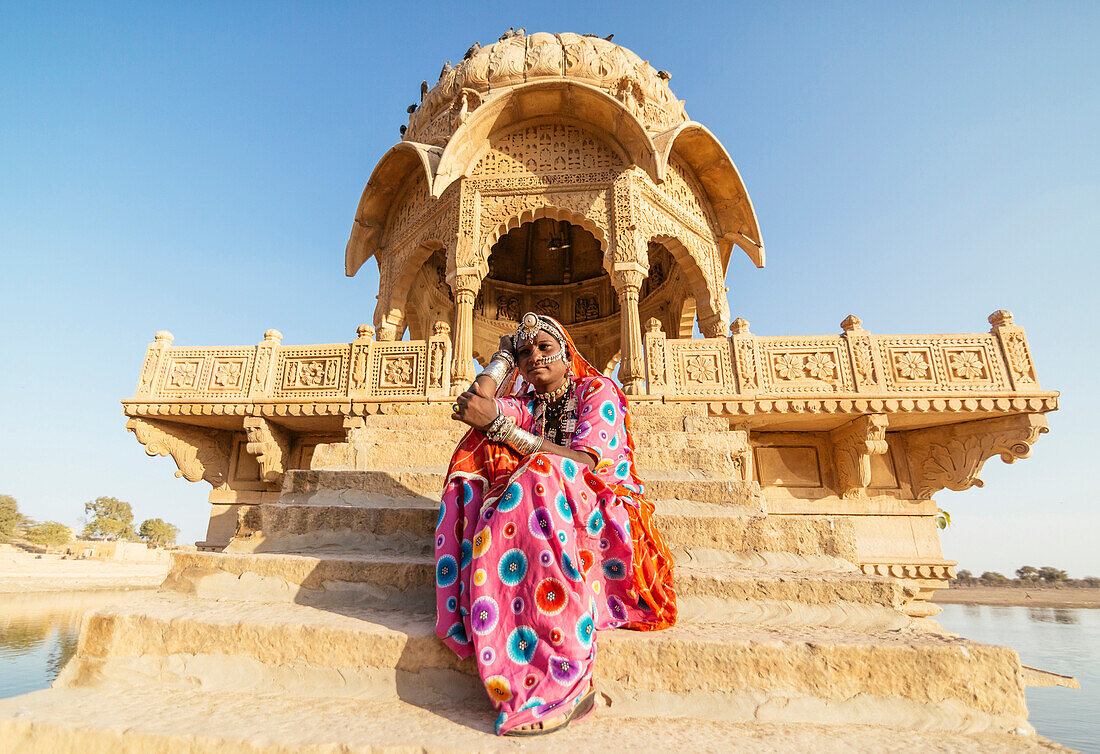Indian woman in traditional clothes sitting near monument, Jaisalmer, Rajasthan, India
