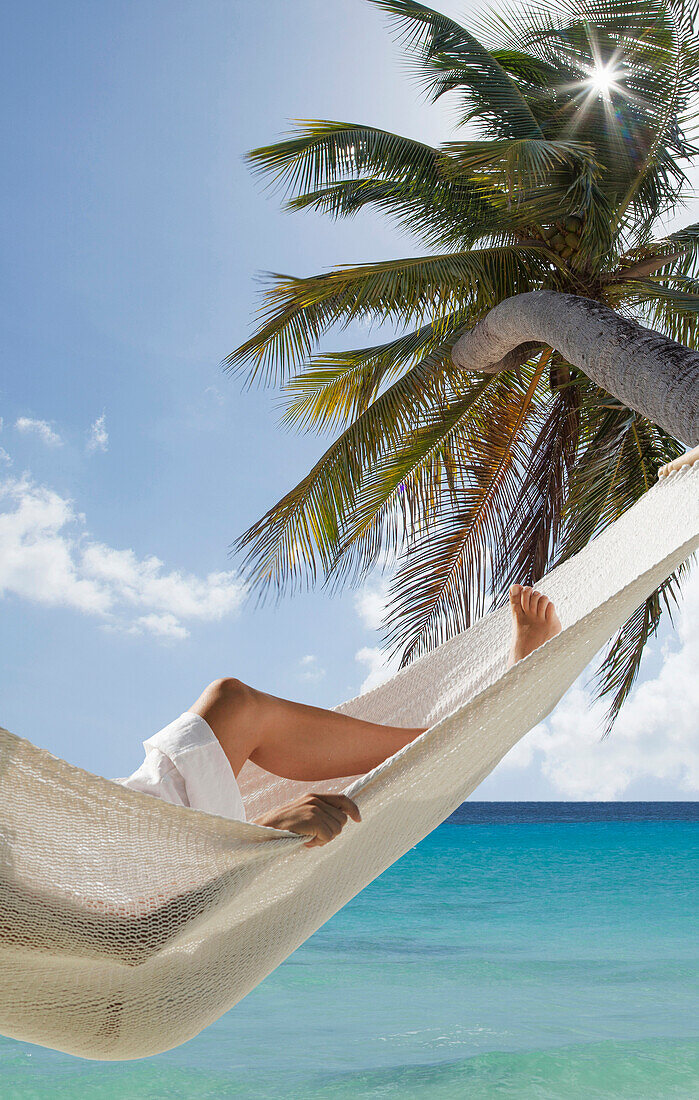 Caucasian woman laying in hammock under palm tree near ocean