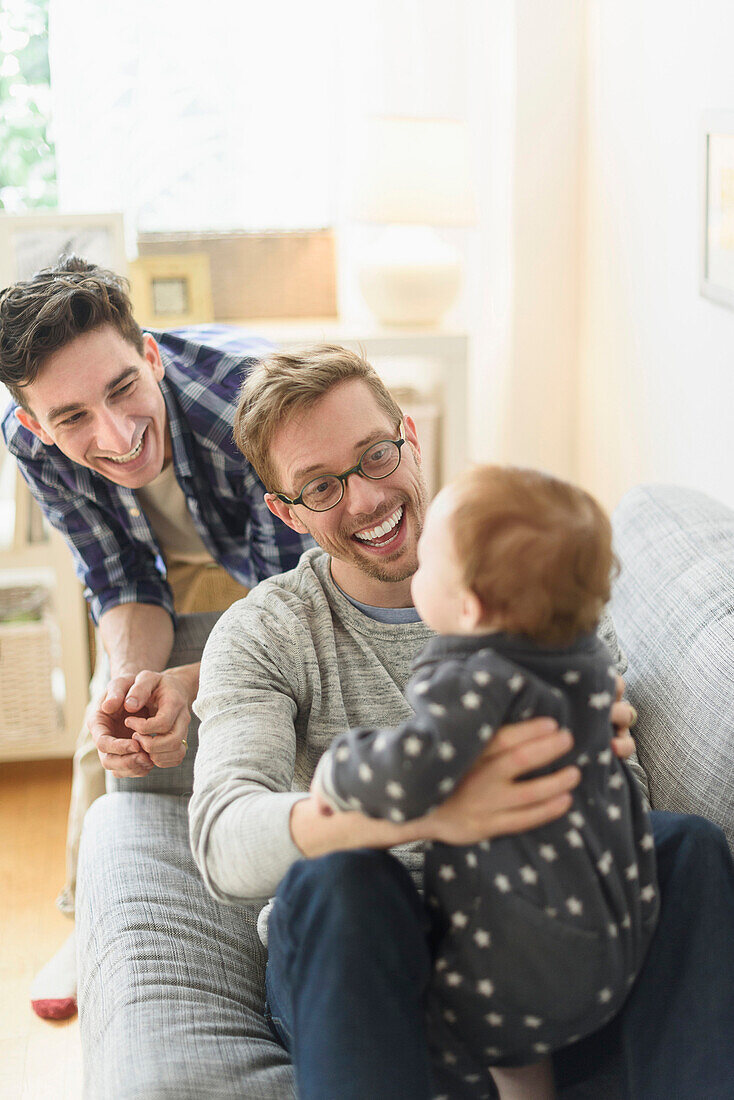 Caucasian gay fathers and baby relaxing on sofa