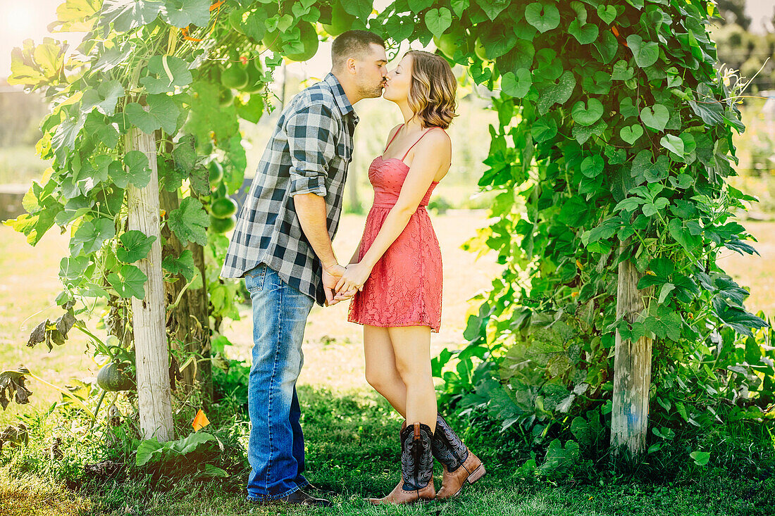 Caucasian couple kissing under leafy arch