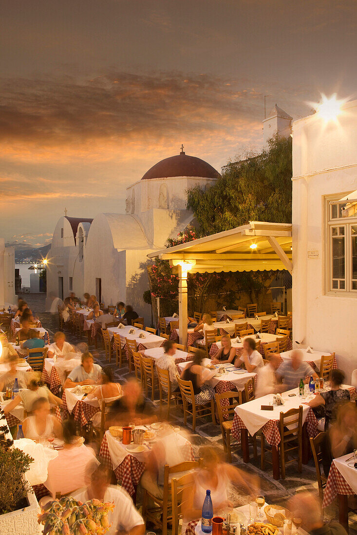 Time lapse view of tourists eating in sidewalk cafe at sunset, Mykonos, Cyclades, Greece