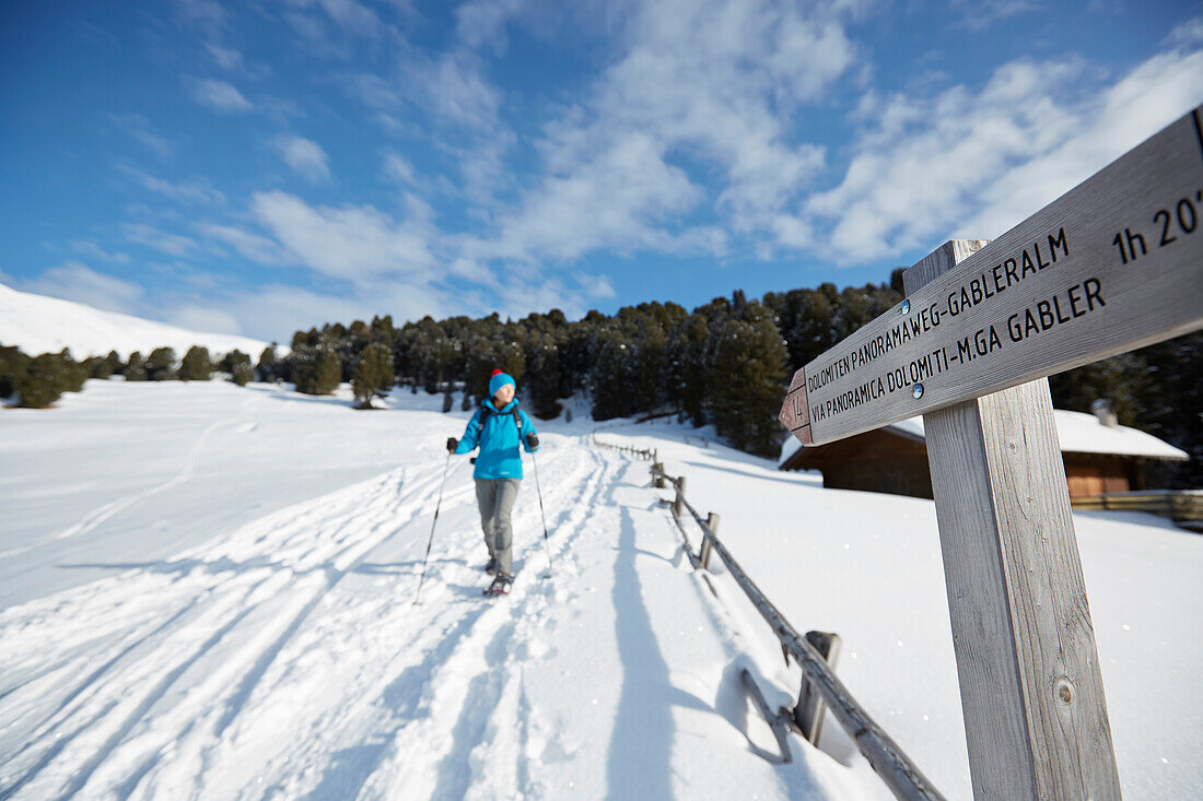 Person snow shoeing in front of signpost, Kreuzwiesenalm, Luesen, South Tyrol, Italy