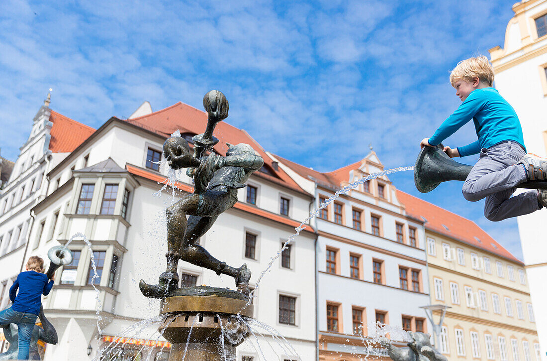 Junge sitzt auf einer Brunnenfigur am Brunnen vor dem Rathaus, Torgau, Sachsen, Deutschland, Europa