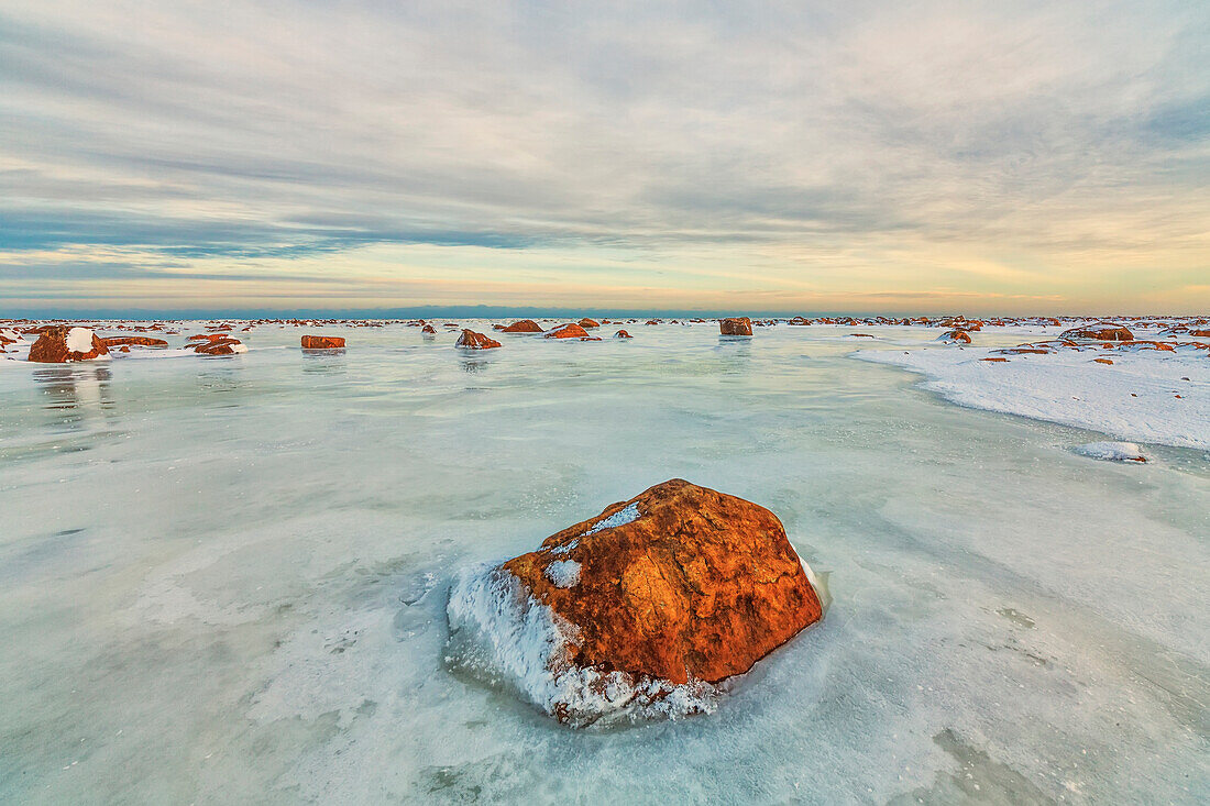 Sunset lights up the rocks and ice covered Hudson Bay, Manitoba, Canada
