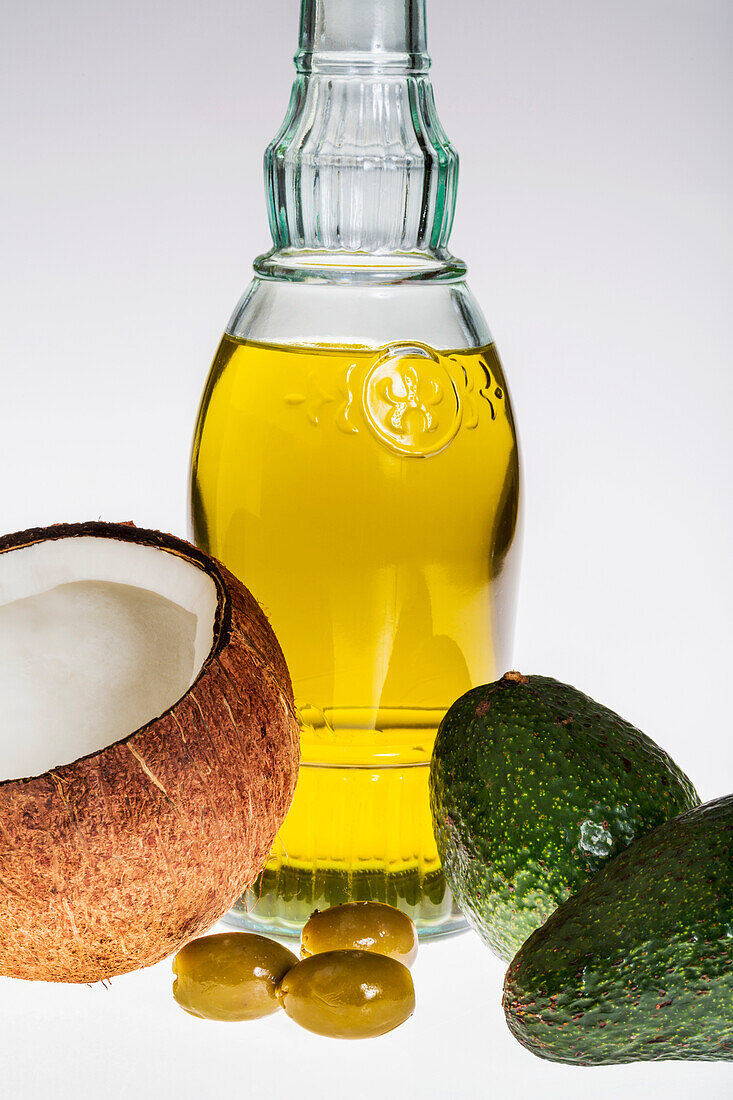 Close up of a coconut, olives, avocados, and glass bottle of olive oil on a white background, Calgary, Alberta, Canada