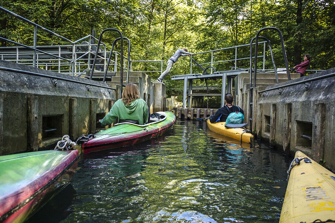 Kajak-Touristen warten in der Schleuse auf die Weiterfahrt auf einem Kanal im Spreewald. Wasser strömt in die Schleuse. Junger Mann öffnet die Schleuse mit Muskelkraft - Brandenburg, Schlepzig, Biosphärenreservat