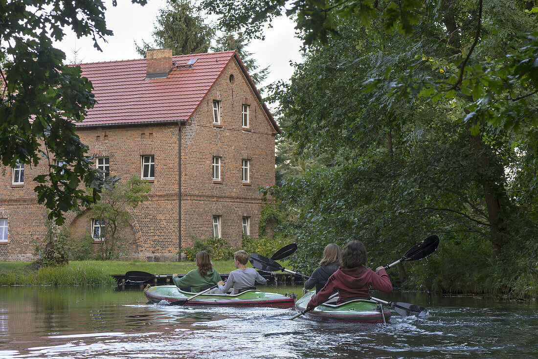 Kajak-Touristen paddeln an einem Backstein-Haus eines Dorfes vorbei, Biosphärenreservat, Schlepzig, Brandenburg, Deutschland
