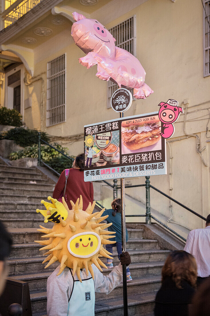 verkleideter Mann hält Schild mit Werbung für ein Restaurant in der Altstadt von Macau, China, Asien