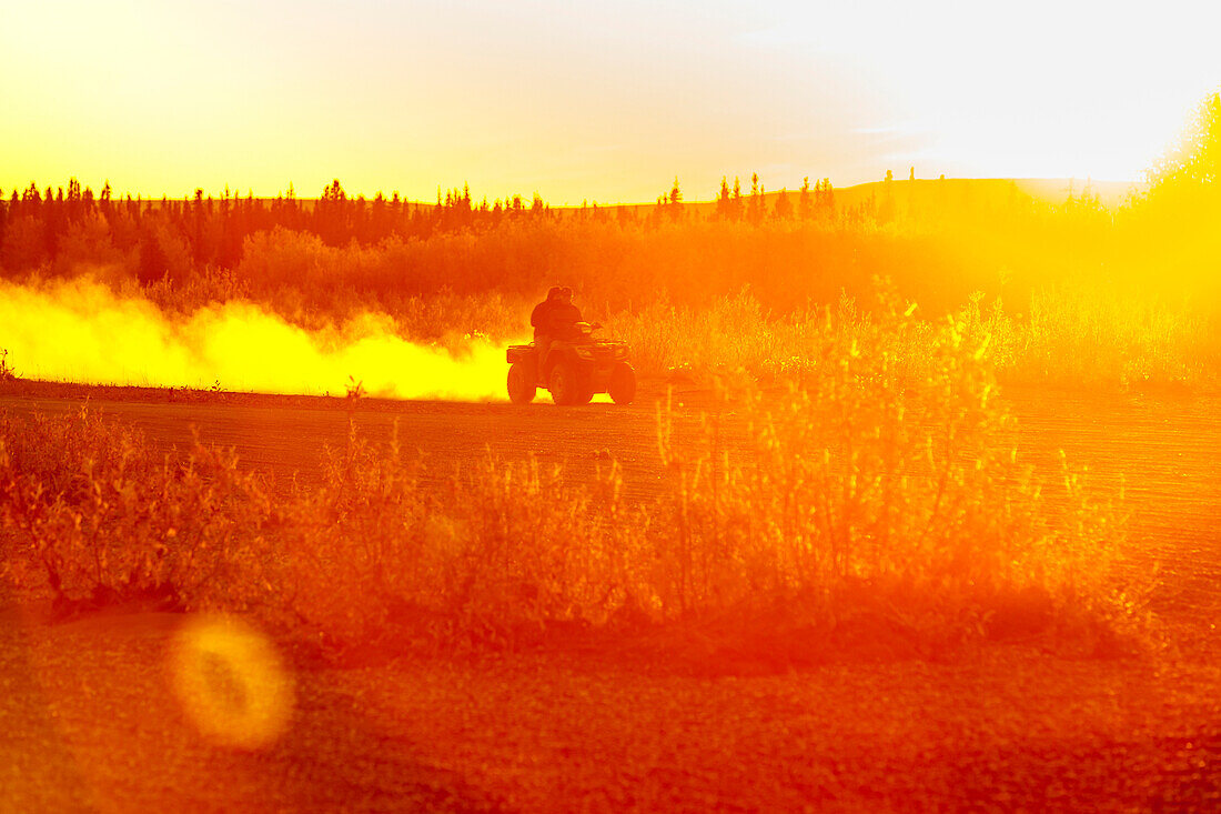 A native Alaskan drives an ATV down a dusty road on the banks of the Noatak River at sunset, Noatak, Arctic Alaska, USA