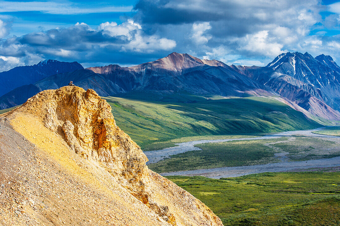 A couple sitting on a rock ledge taking in the view at Polychrome Pass in Denali National Park, Interior Alaska
