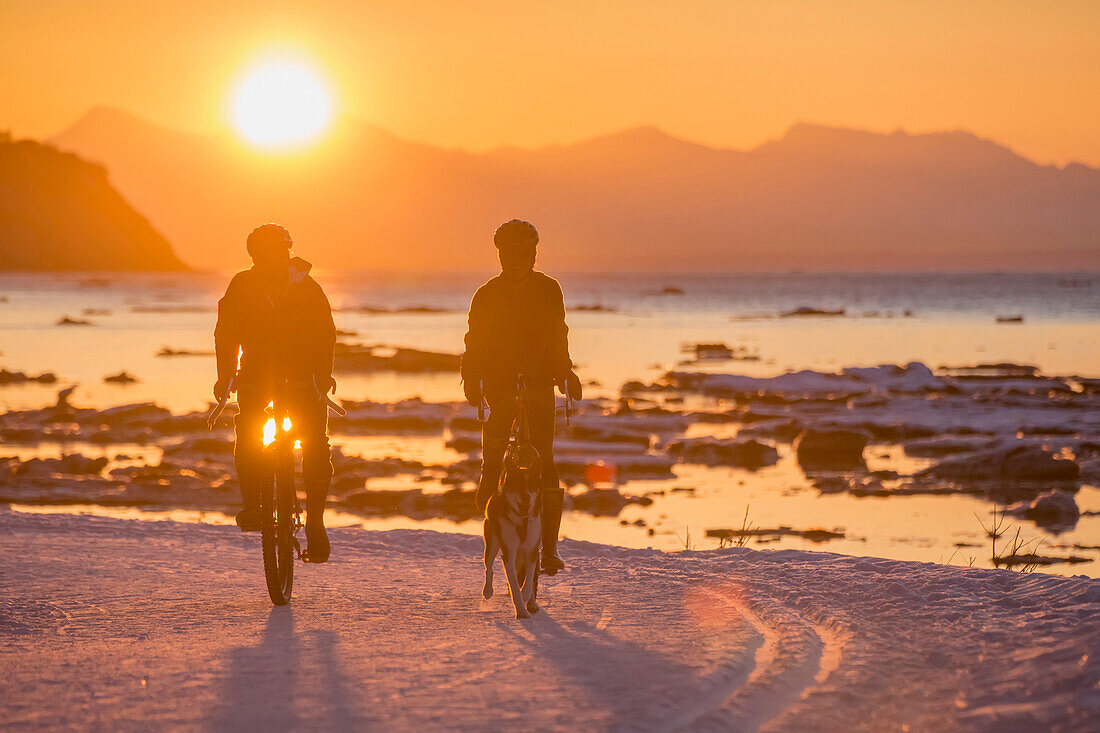 Couple bicycling in winter at sunset on the Tony Knowles Coastal Trail, Cook Inlet, Southcentral Alaska