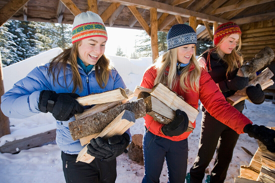 Three Young Women Collect And Pile Chopped Wood Near Homer, Alaska During Winter.