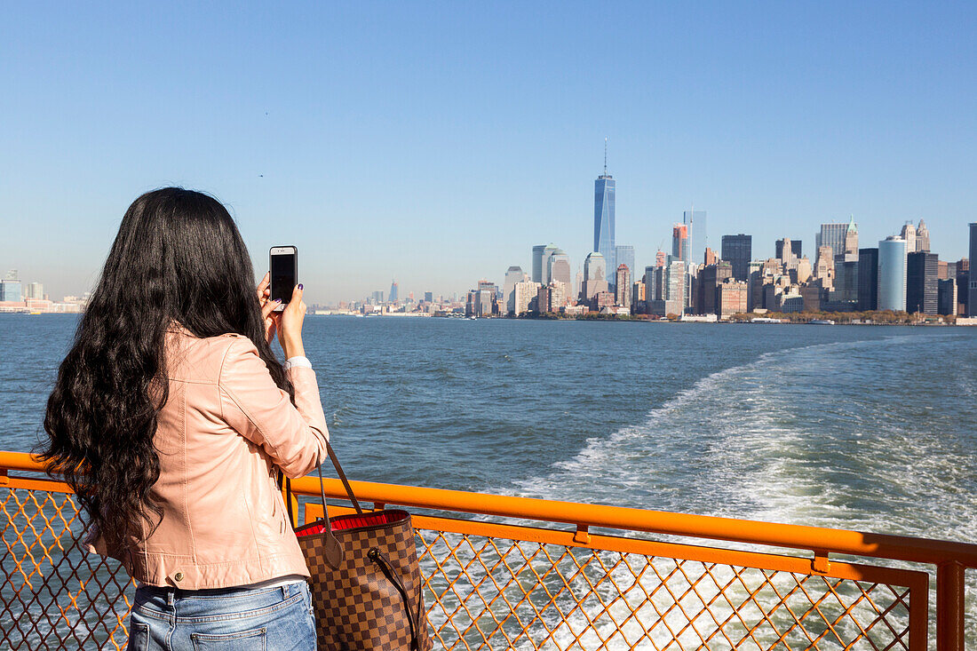 Asiatin, Smartphone, Frau fotografiert mit Handy, Fähre von Manhattan nach Staten Island, Blick auf downtown Manhattan und das neue One World Trade Center, New York City, USA, Amerika