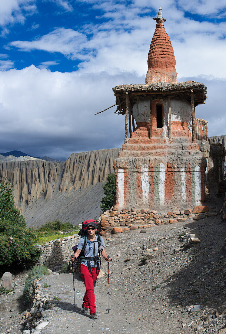 Young woman, trekker walking in front of a Buddhist stupa, Tangge, tibetian village with a buddhist Gompa in the Kali Gandaki valley, the deepest valley in the world, Mustang, Nepal, Himalaya, Asia