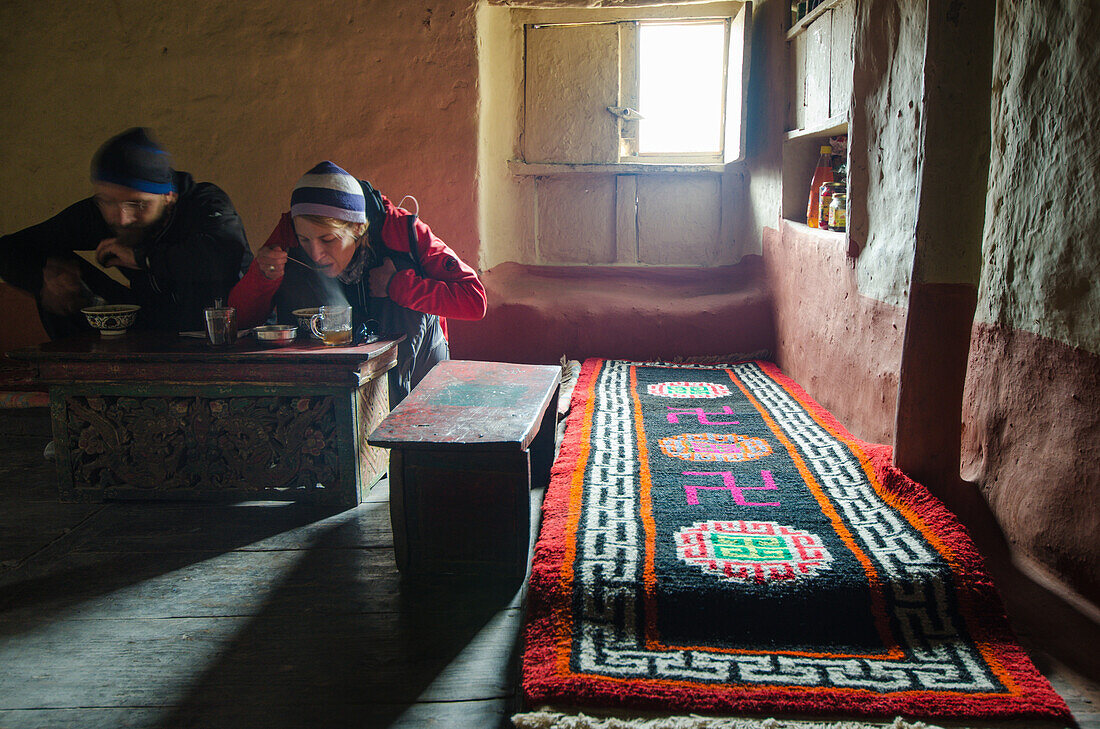 Ein junger Mann und junge Frau essen in typisch tibetischem Wohnzimmer, Haus in Lupra, kleine Ortschaft mit buddhistischem Kloster im am Kali Gandaki Tal, dem tiefsten Tal der Welt, Mustang, Nepal, Himalaya, Asien