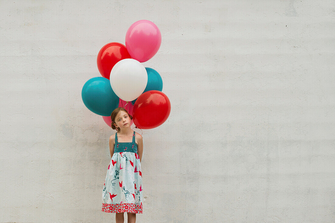 Caucasian girl holding bunch of balloons