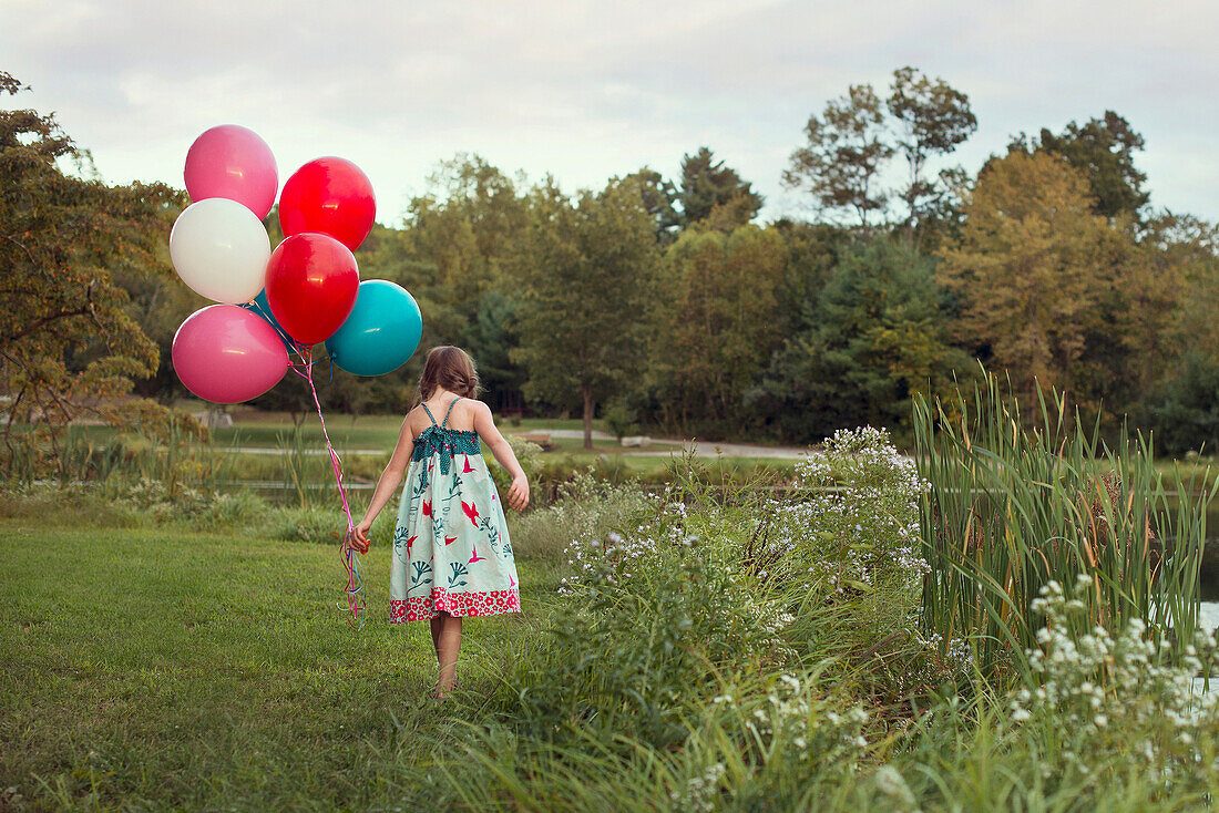 Caucasian girl carrying balloons in rural field
