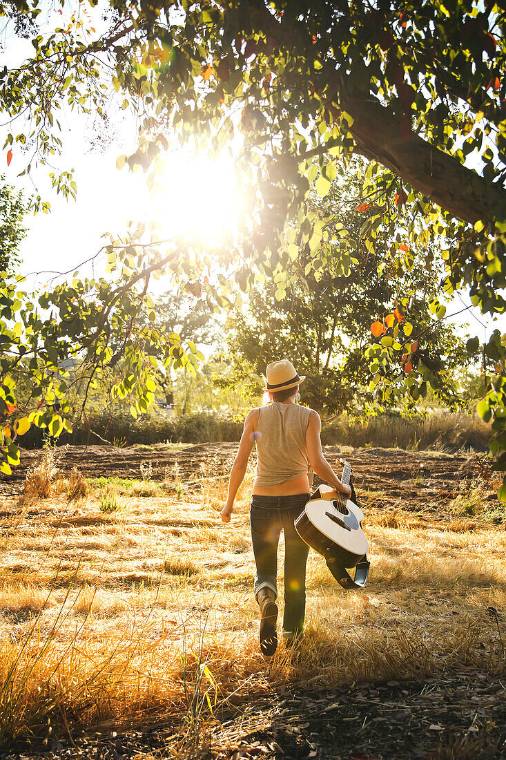 Caucasian musician carrying guitar in rural field