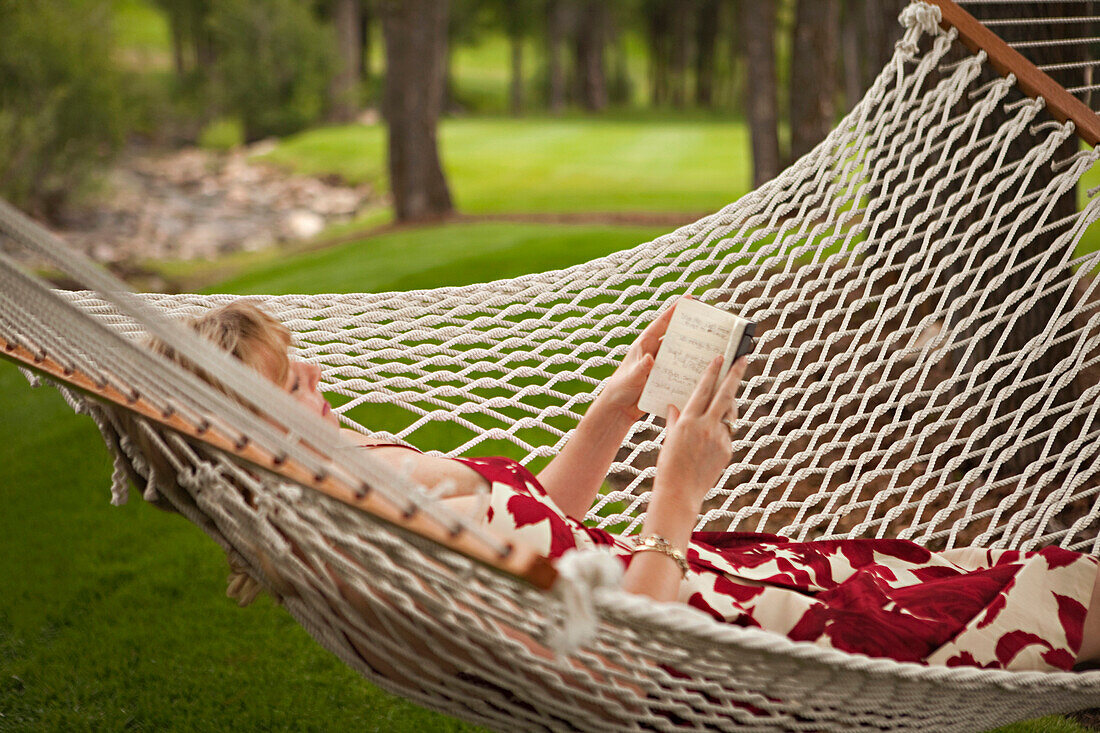Woman reading book in backyard hammock