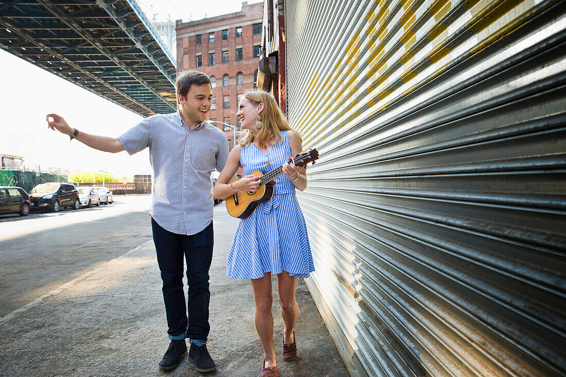 Caucasian couple playing ukulele on city sidewalk