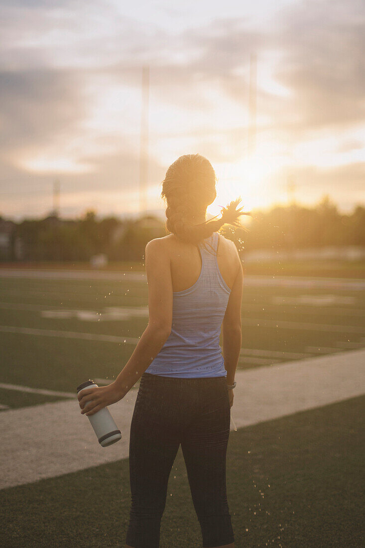 Gemischtrassige Athletin mit Wasserflasche auf einem Sportplatz