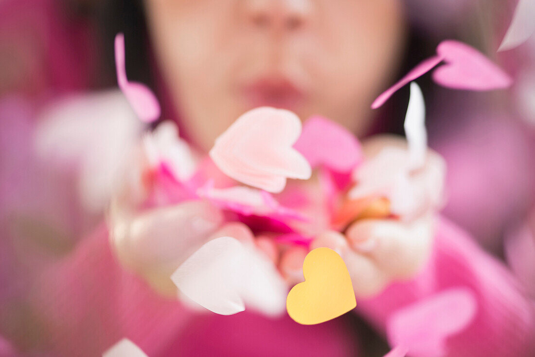 Mixed race woman blowing confetti hearts