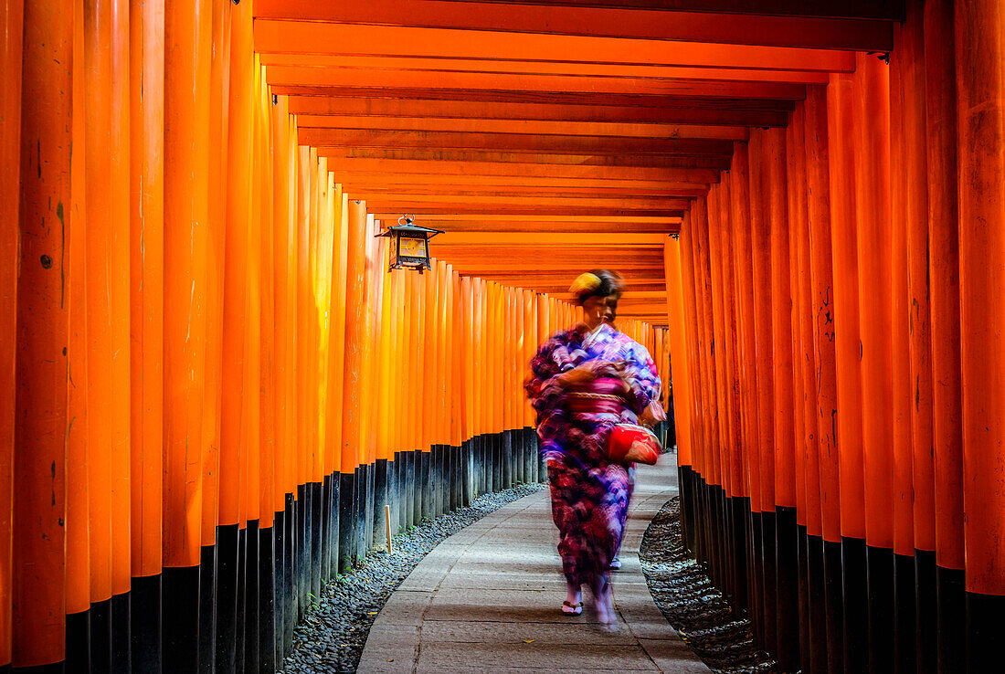 Woman in kimono walking under wooden pillars