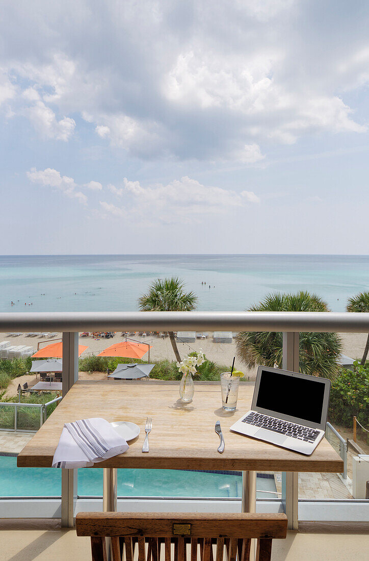 Laptop on restaurant balcony table overlooking beach