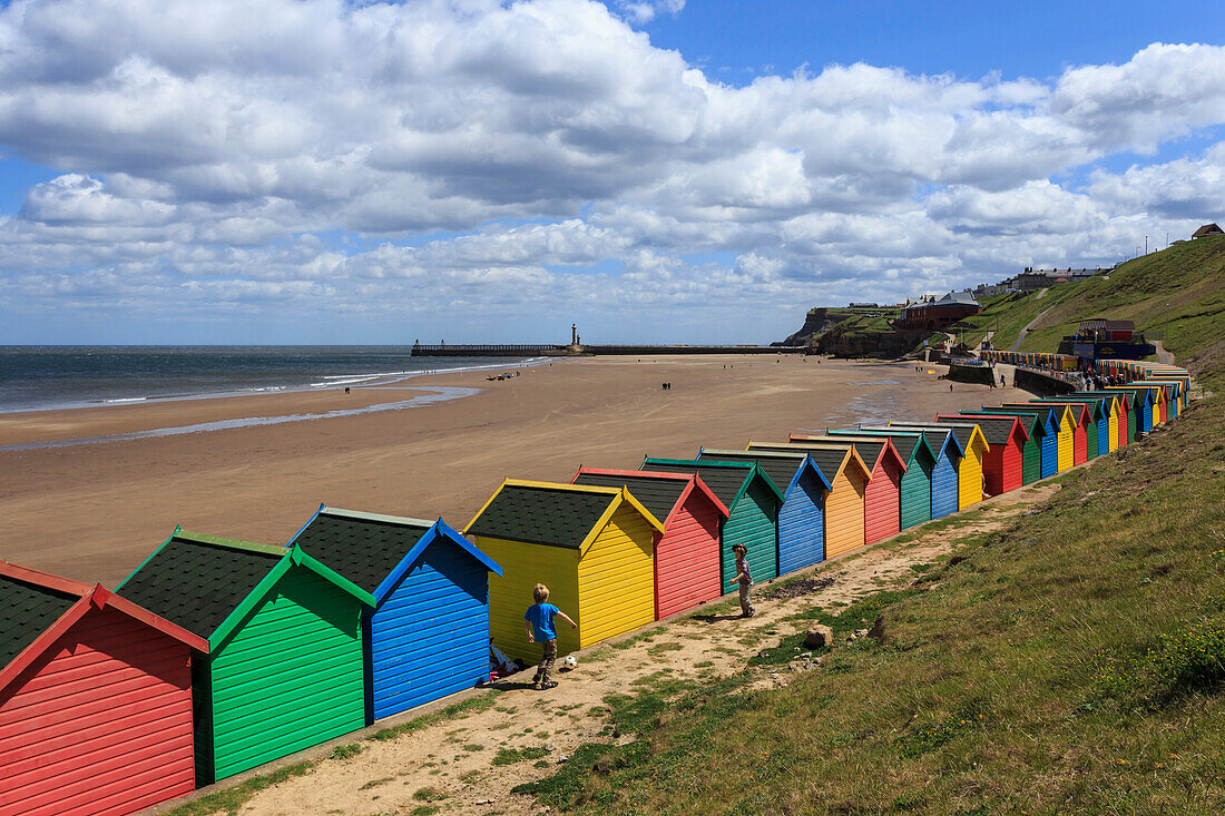 Children kick football near colourful beach huts above West Cliff Beach, Whitby, North Yorkshire, England, United Kingdom, Europe