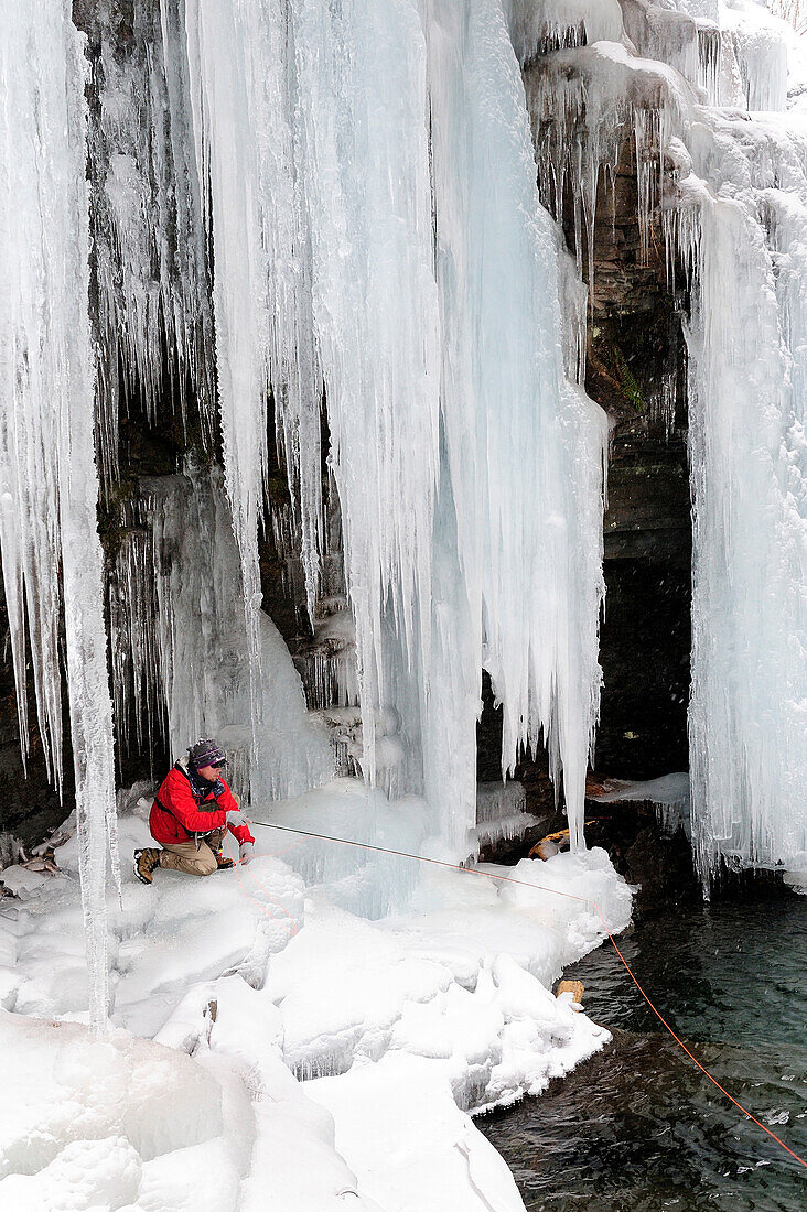 A man fly fishing under icicles on a cold winter day.