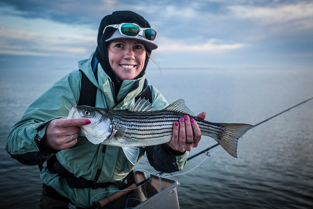 A woman poses with a striped bass she caught while fly fishing on Martha's Vineyard.