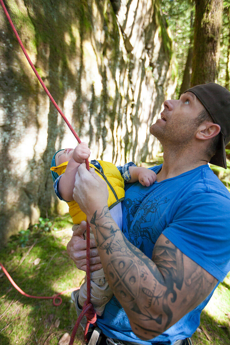 A father and his son reach for a climbing rope while looking up at a climbing route.