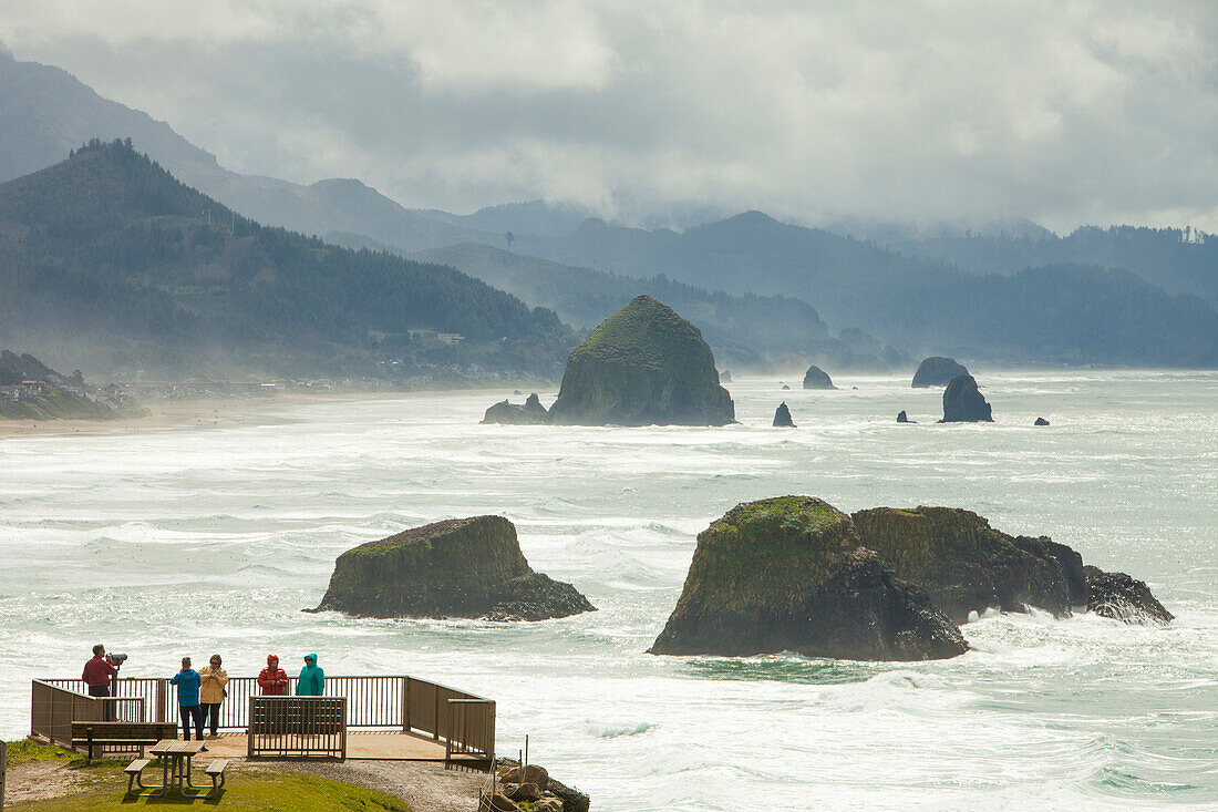 Tourists enjoy the view of Haystack Rock and Cannon Beach looking south from a viewpoint in Ecola State Park, Oregon.