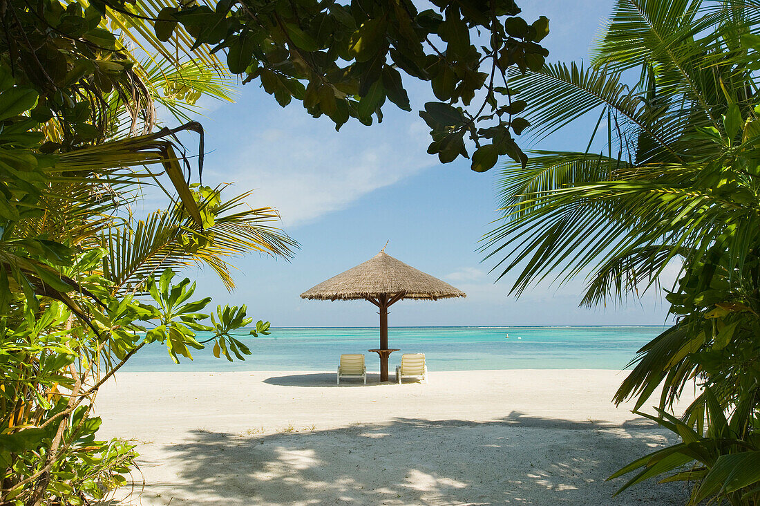 Lounge chairs and a palapa umbrella on the beach at an island resort in South Male Atoll, Maldives.