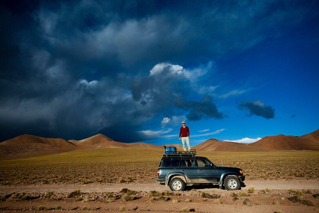 A man stands on the roof of his truck to take a photo of the dramatic sky at sunset near the Salar de Uyuni, Bolivia.