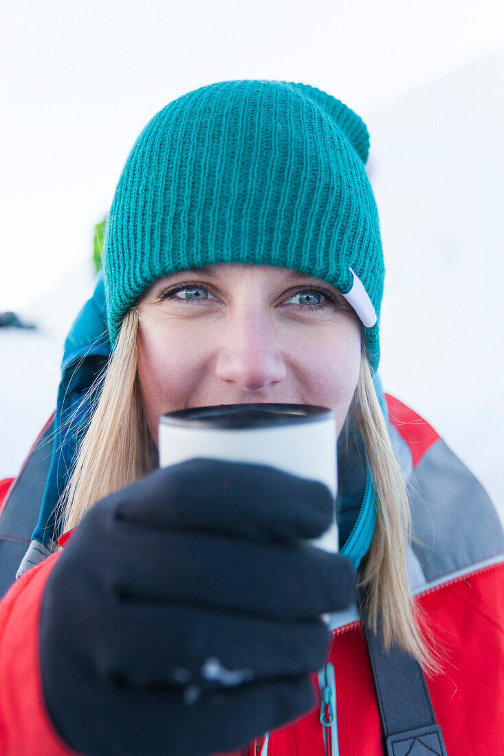 A young active woman enjoys a hot drink during a winter camping trip.