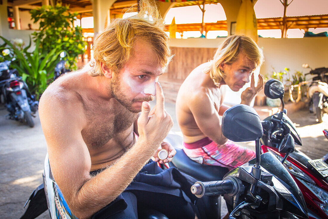 Young men anoint faces protective cream before surf session.