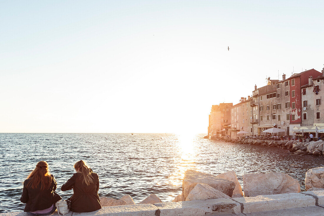 Two young women on a seawall at sunset, Rovinj, Istria, Croatia