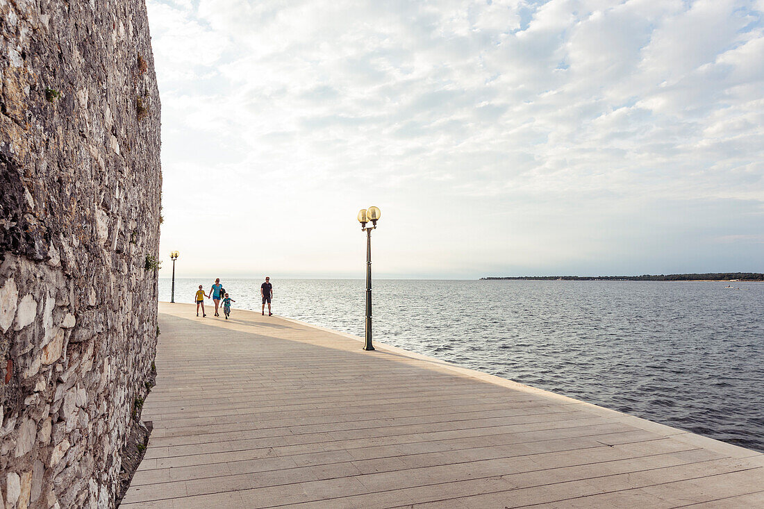 Young family walking along the waterfront of Porec, Istria, Croatia