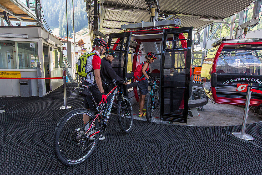 Couple pushing their mountain bikes into a cable car at Ciampioni station, Wolkenstein, Trentino South Tyrol, Italy
