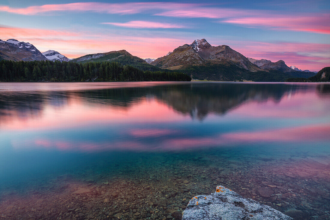 Pink sky at dawn illuminates the peaks reflected in Lake Sils, Engadine, Canton of Graubunden, Switzerland, Europe