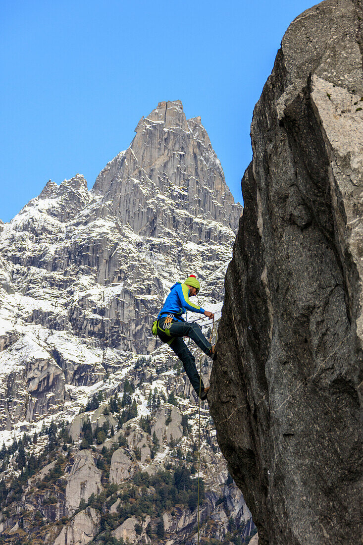 Climber on steep rock face in the background blue sky and peaks of the Alps, Masino Valley, Valtellina, Lombardy, Italy, Europe