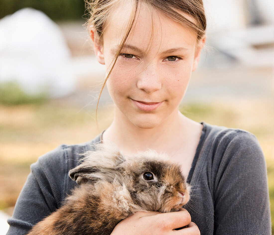 Serious girl holding rabbit on farm
