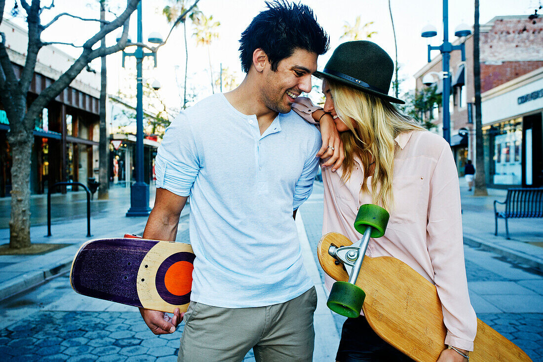 Caucasian couple carrying skateboards