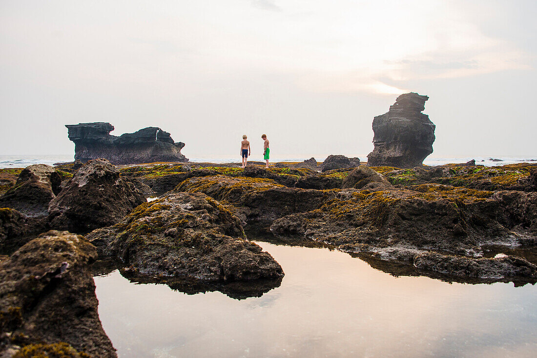 Caucasian children exploring rocky tidal pools, Canggu, Bali, Indonesia