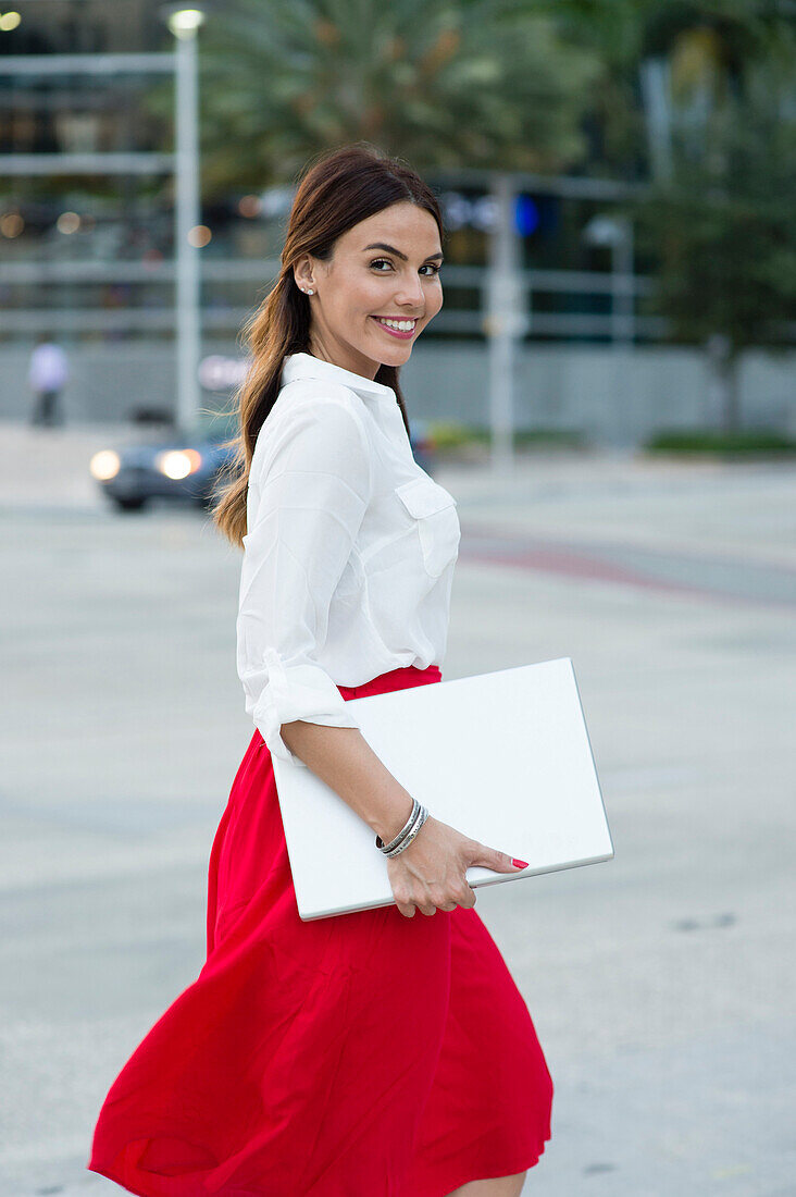 Hispanic businesswoman carrying laptop outdoors