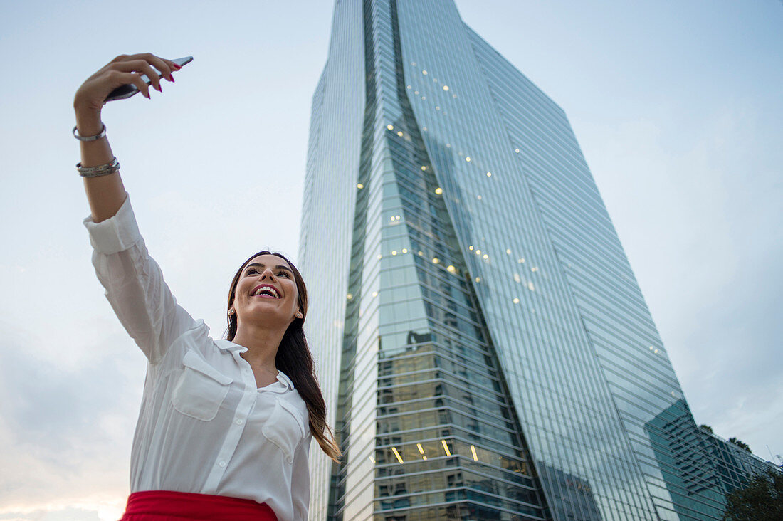 Hispanic businesswoman taking selfie outdoors