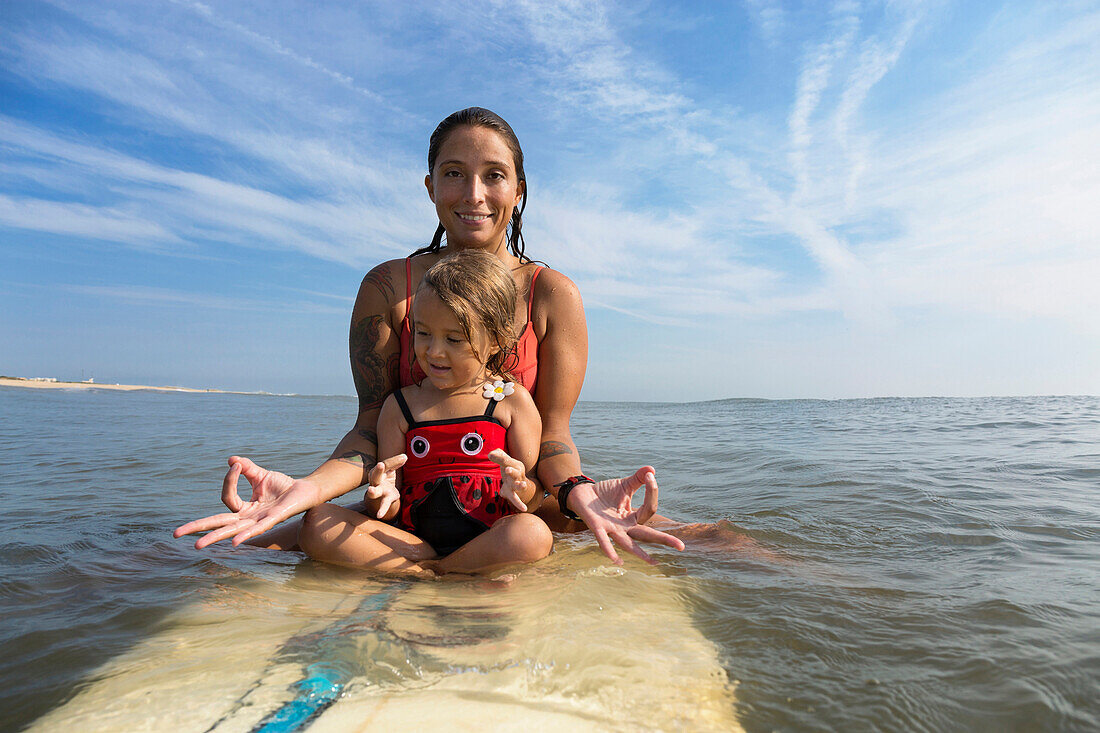 Mutter und Tochter meditieren auf einem Surfbrett