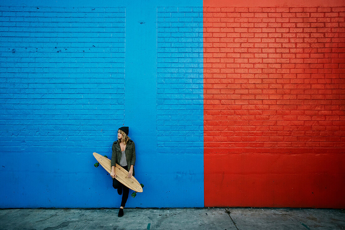 Caucasian woman holding skateboard at painted wall