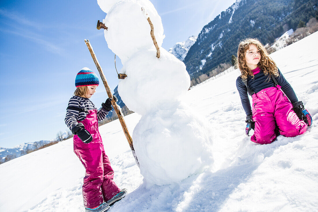 Mädchen und Junge bauen einen Schneemann im Winter, Pfronten, Allgäu, Bayern, Deutschland